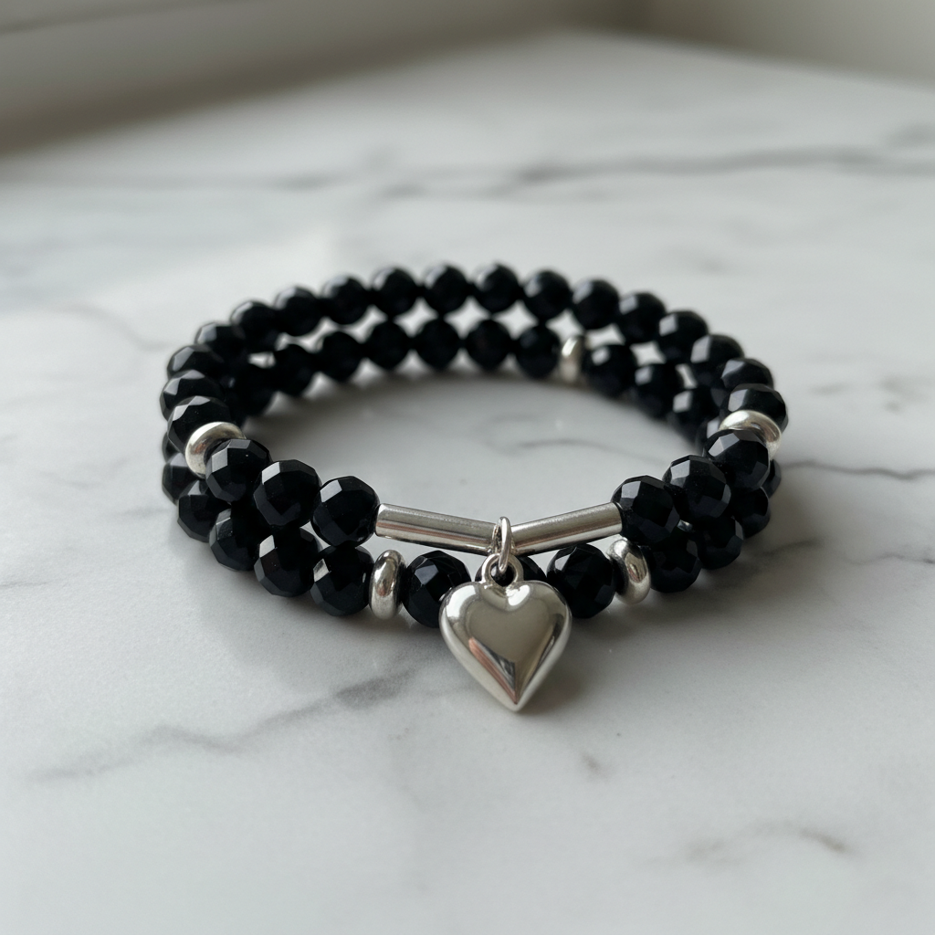 Black beaded heart charm stretch bracelet with silver accents on marble surface