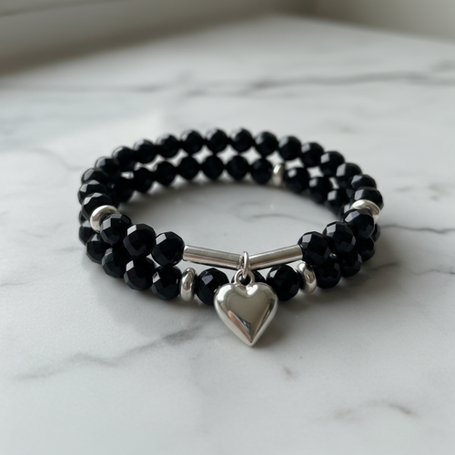 Black beaded heart charm stretch bracelet with silver accents on marble surface